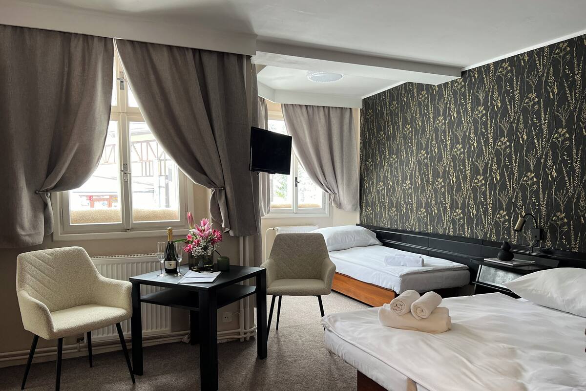 A hotel room with a bed, a desk with a chair, a TV, and a window with curtains.