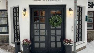 A white building with a black door, labeled "LOMNICE hotel & restaurant," featuring a wreath and potted plants.