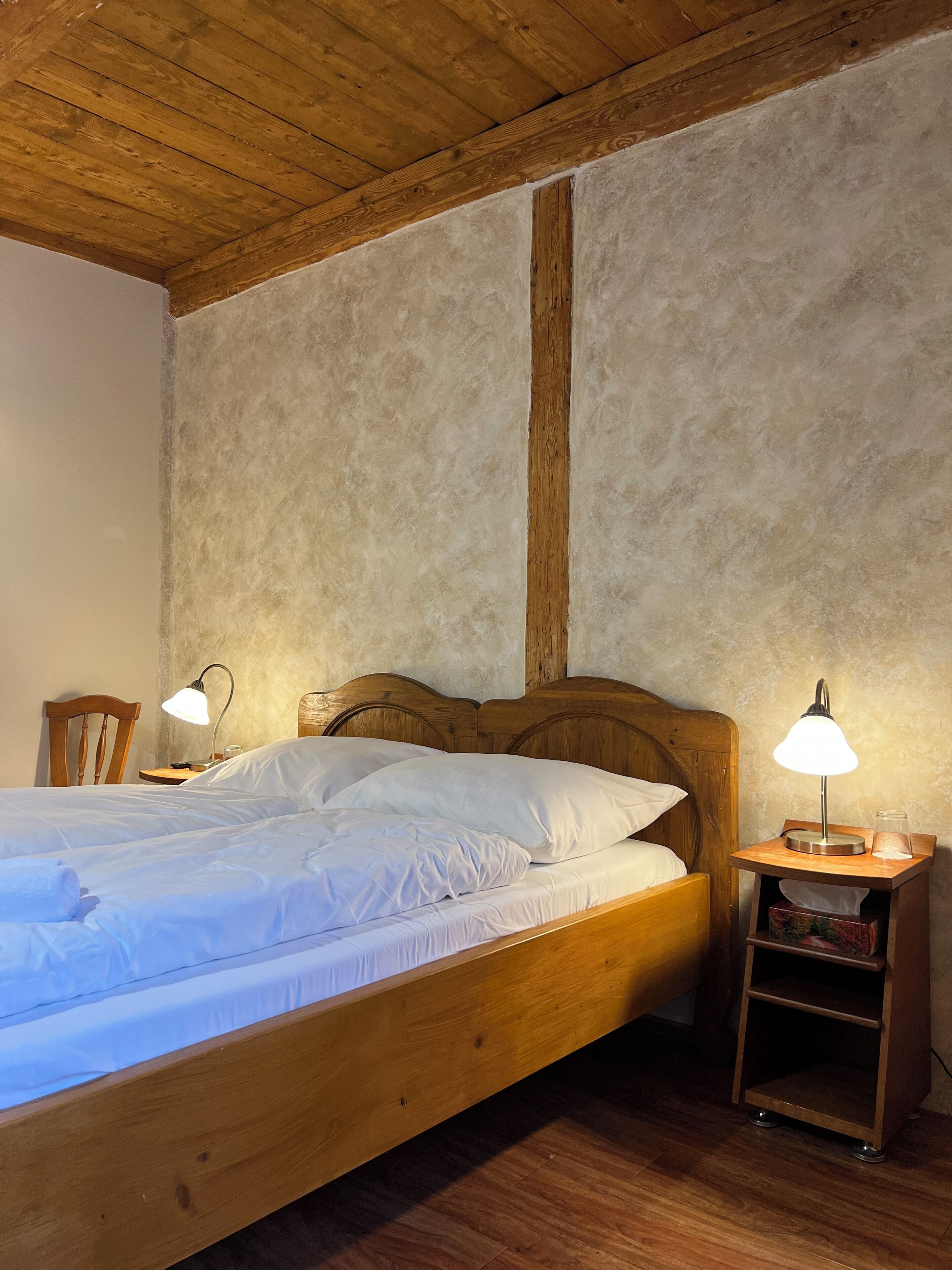 A wooden bed with white bedding, two bedside lamps, and a wooden nightstand with a shelf.