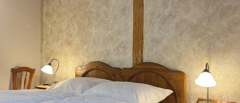 A wooden bed with white bedding, two bedside lamps, and a wooden nightstand with a shelf.