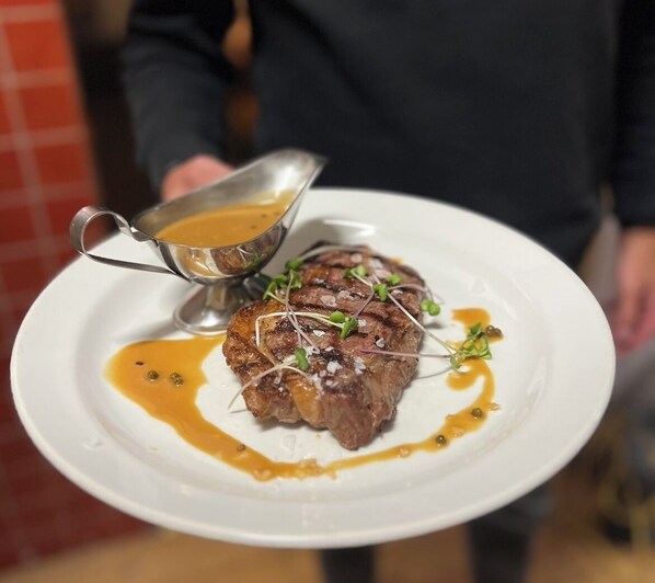 Una persona sosteniendo un plato con un bistec, salsa y vegetales verdes.