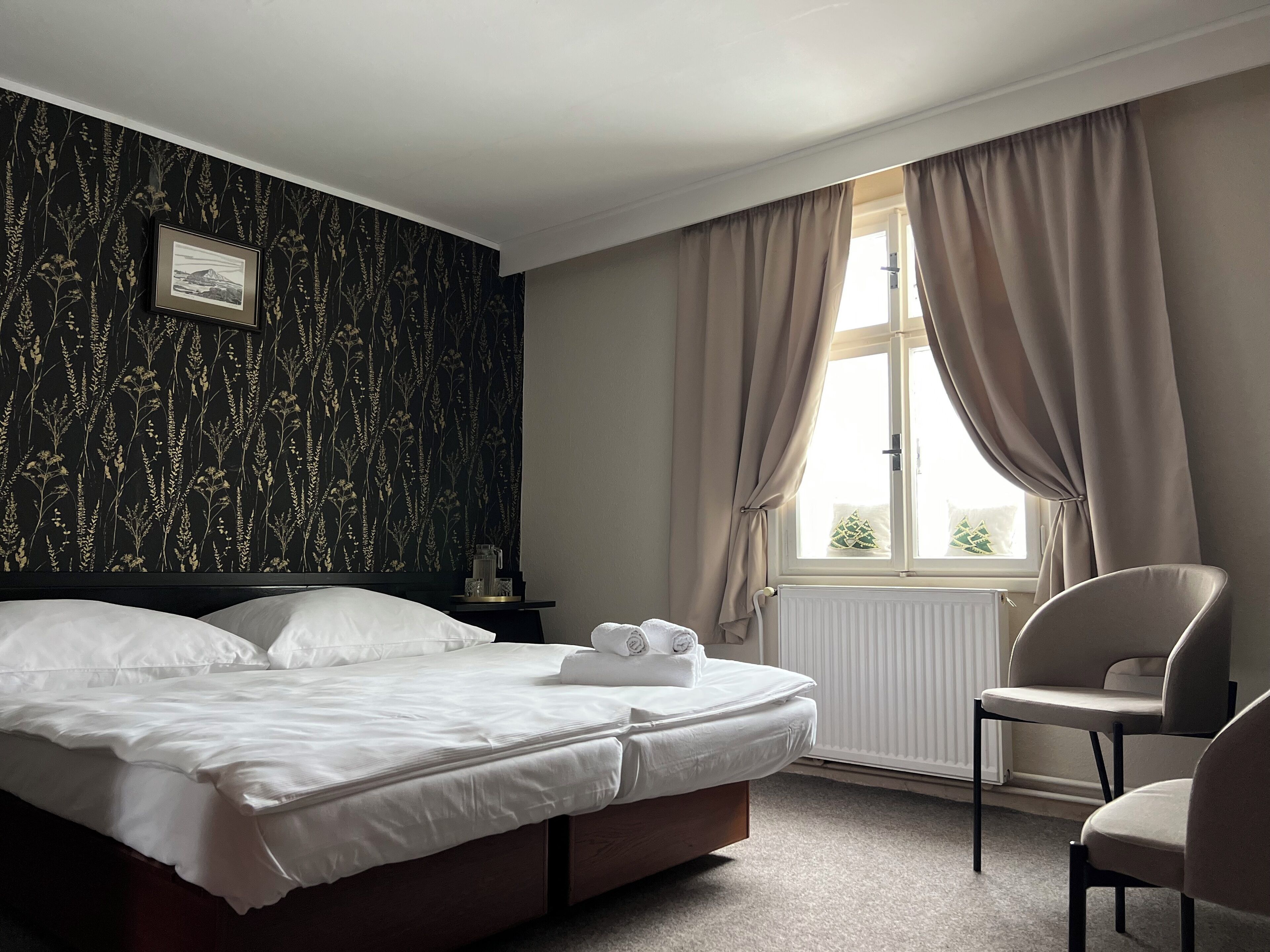 A neatly made bed with white linens, a framed picture on the wall, and a window with curtains.