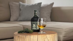 Un taburete de madera con una botella y un vaso, colocado frente a un sofá.