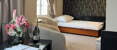 Una habitación de hotel con una cama, un escritorio con un florero, una botella de champán y un cuadro en la pared.