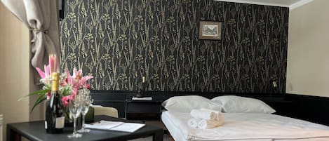 Habitación de hotel con cama, escritorio con lámpara, silla y una pequeña mesa con un jarrón de flores.