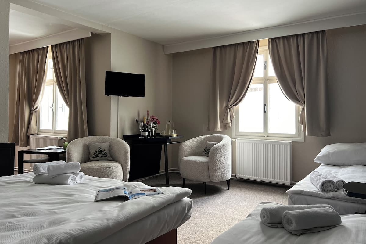 A hotel room with two beds, a chair, a desk with a flat-screen TV, and a window with curtains.