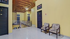 A hallway with a tiled floor, wooden ceiling, and black doors numbered 8, 10, 12, and 13. There are two patterned chairs and a metal railing. - Hotel O Arafah Homestay Syariah Near Badan Pertanahan Nasional - Kantor Pertanahan Kabupaten Kampa (Bangkinang)