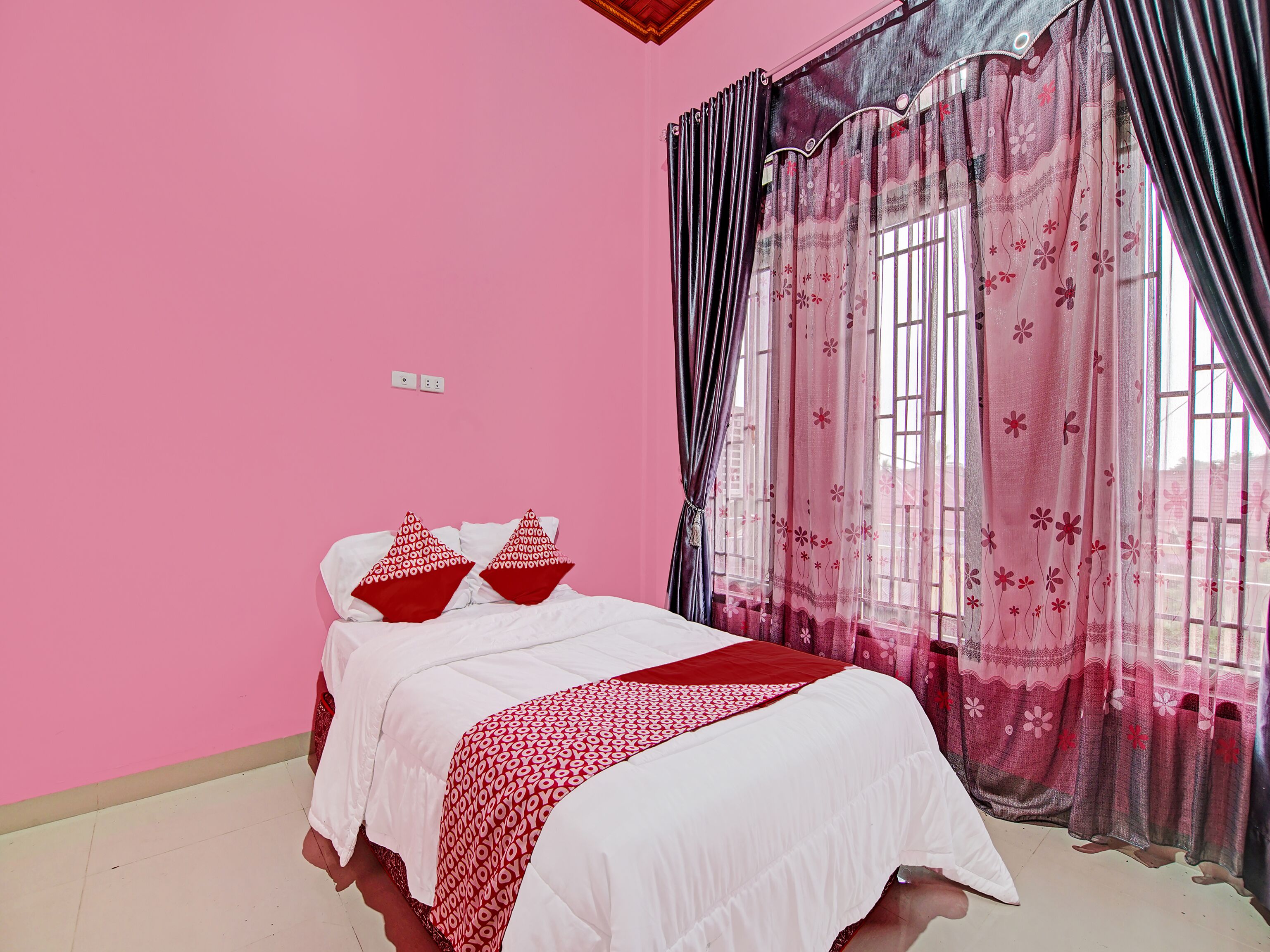 Een slaapkamer met een bed, roze wanden en bloemen gordijnen.