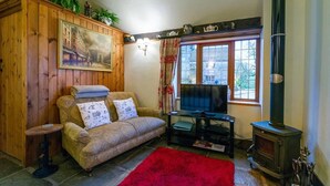 Ein gemütliches Wohnzimmer mit einer Couch, einem Fernseher, einem Kamin und einem Fenster mit Vorhängen.