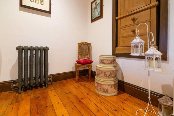 Une pièce avec un radiateur, une chaise en bois dotée d’un coussin rouge, une pile de récipients cylindriques et une lanterne blanche posée sur un pied.