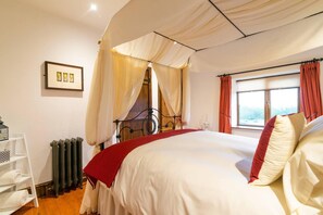 Un dormitorio con cama a dosel, un radiador, un estante blanco con toallas y una ventana con cortinas.