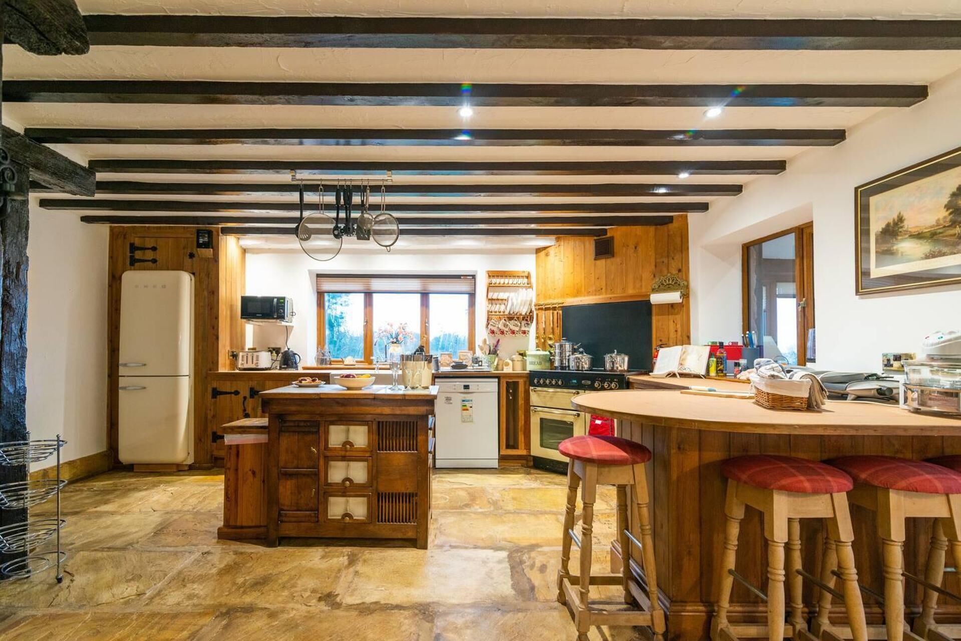 Una cocina rústica con vigas de madera, una isla central con taburetes, un refrigerador y vistas al exterior.