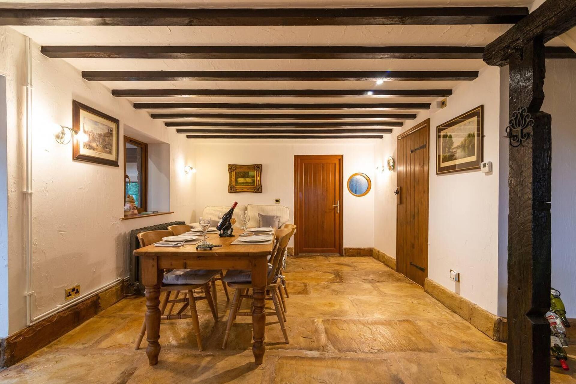 Una sala da pranzo con un tavolo di legno apparecchiato per quattro persone, circondato da sedie, un pavimento in pietra e travi a vista sul soffitto.