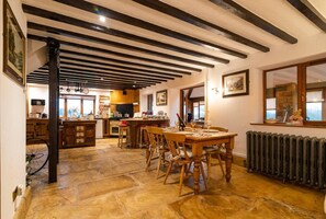 Una cocina amplia con vigas de madera, un comedor con una gran mesa de madera y un suelo rústico de piedra.