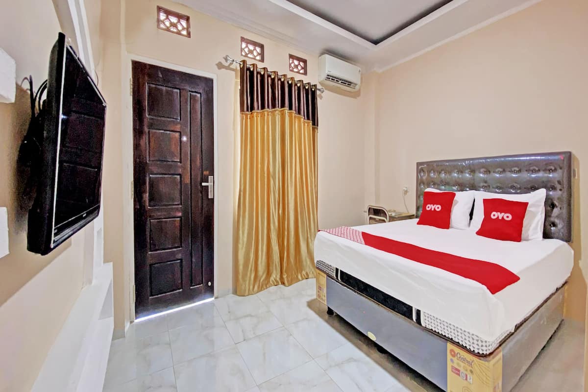 A hotel room with a bed, a television, a door, and an air conditioning unit.