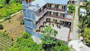 Un edificio de varios pisos con un balcón en la planta baja, rodeado de vegetación y otros edificios residenciales.