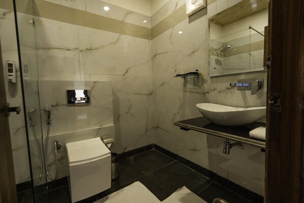 A modern bathroom with a glass-enclosed shower, a white toilet, a black sink, and a mirror above the sink. - Anantum Gateway Resorts (Ramnagar)