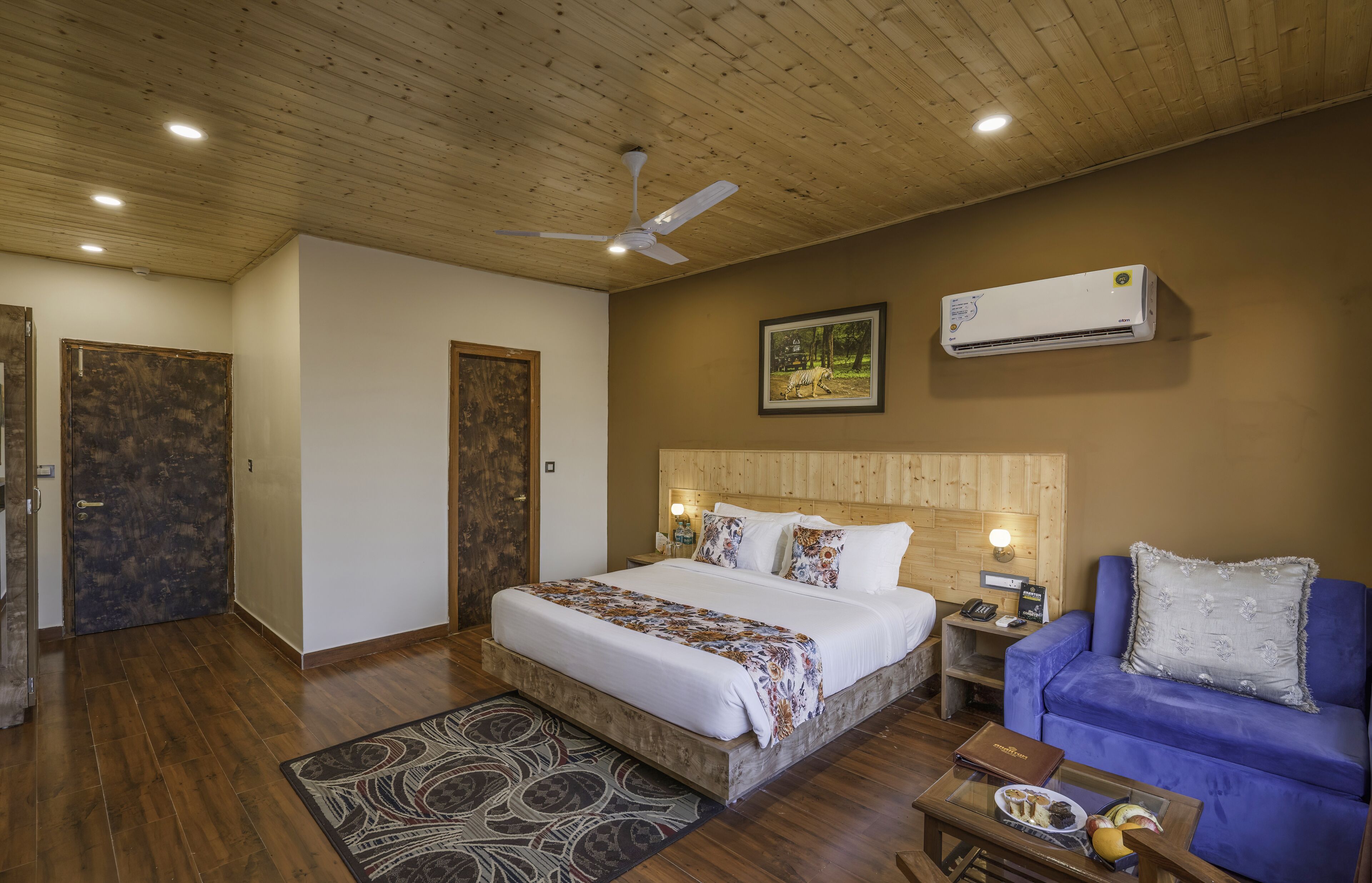 A bedroom with a wooden ceiling, a bed with a patterned bedspread, a blue sofa, and an air conditioning unit.