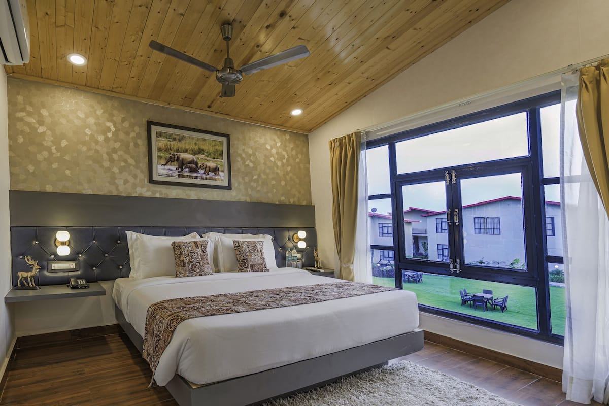 A bedroom with a large bed, a ceiling fan, a nightstand with a phone, and a window with curtains.