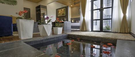 A hotel lobby with a central water feature, a seating area, and a large window with curtains.