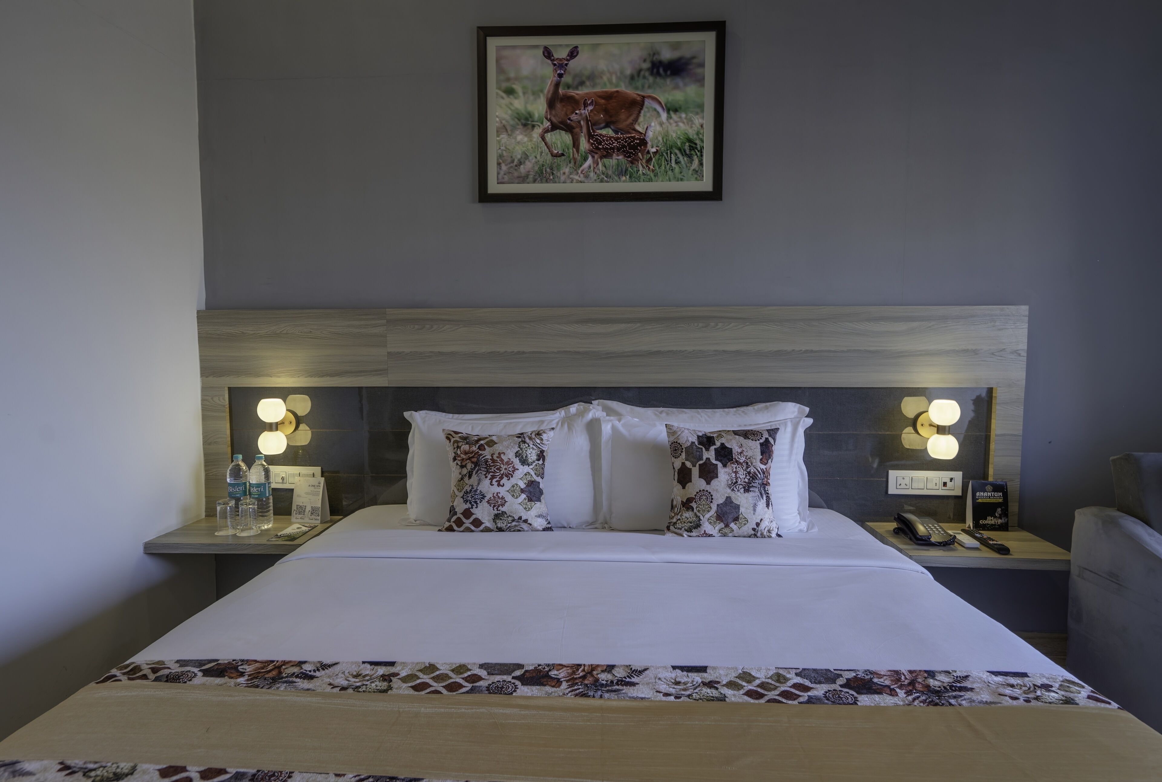 A neatly made bed with patterned pillows, a framed picture above, and bedside tables with lamps and a phone.