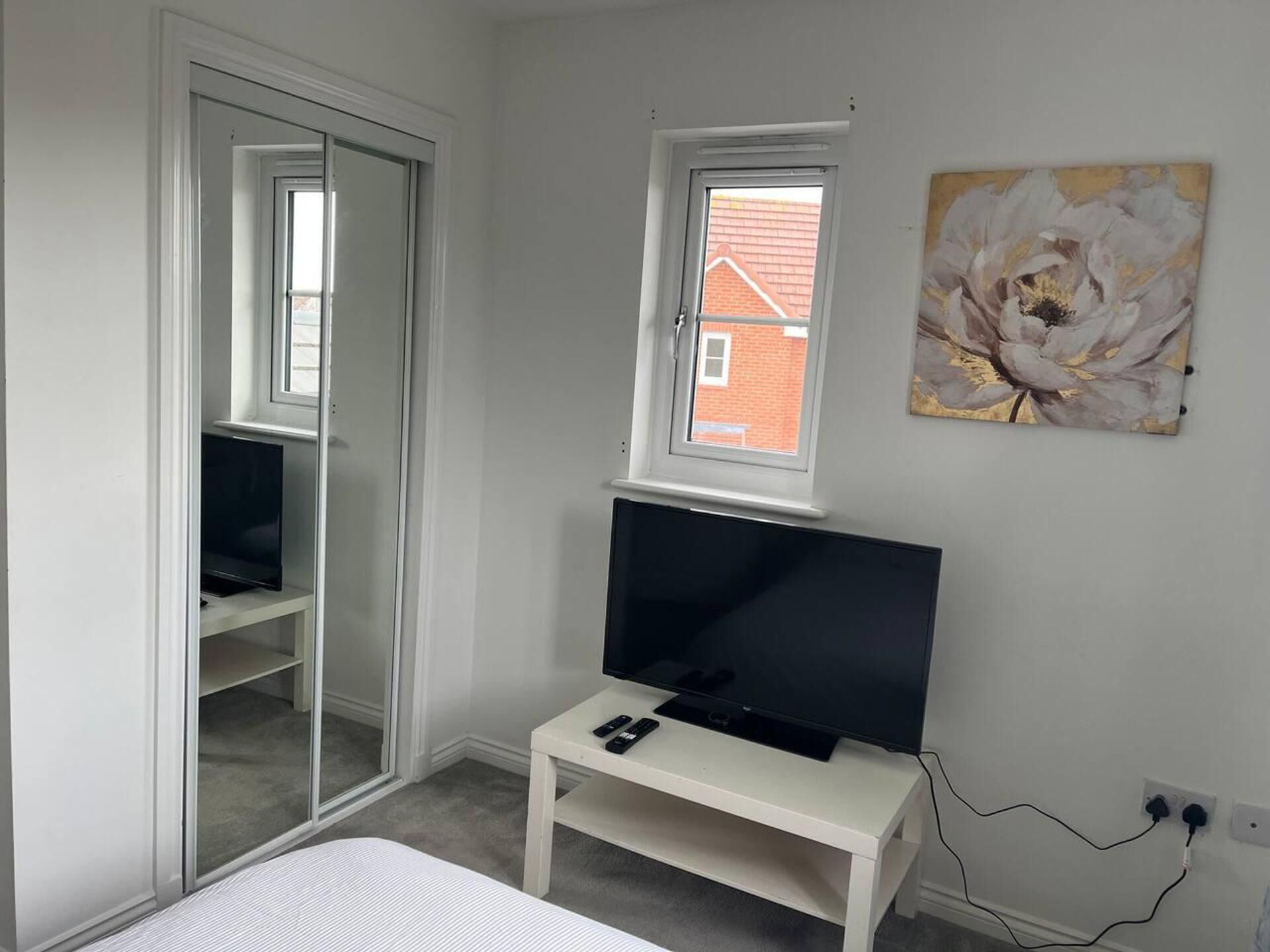 A bedroom with a bed, a TV on a stand, a window, and a painting on the wall.