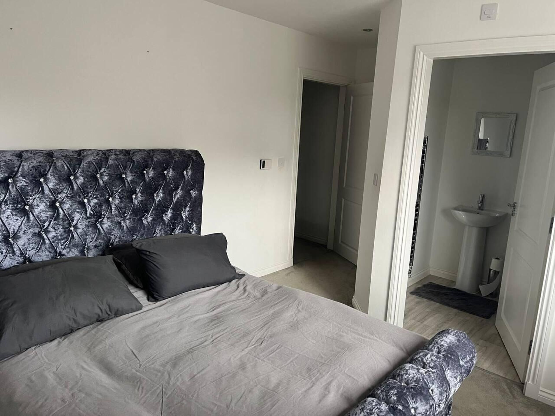 A bedroom with a tufted headboard, a grey bedspread, and a matching bench.