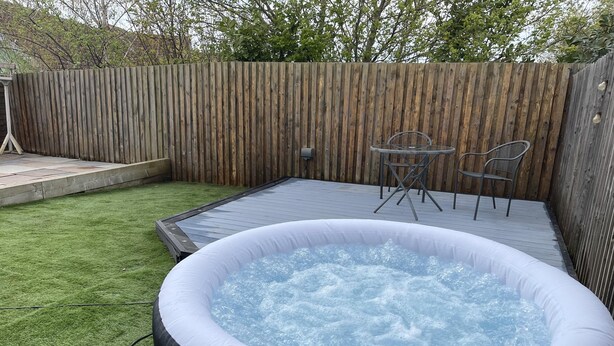 An inflatable hot tub in a backyard with a wooden deck, a small table, and two chairs. - Remarkable 3-bed House in Wirral (Wirral)