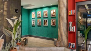 A lobby with a green wall, framed artwork, a red bookshelf, and potted plants. - Azuu Bohem (Antalya)