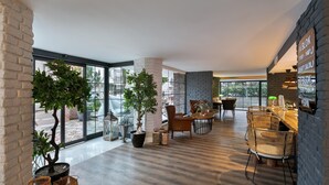A modern interior with large windows, wooden flooring, and a mix of seating areas including a bar and a dining table. - Azuu Bohem (Antalya)