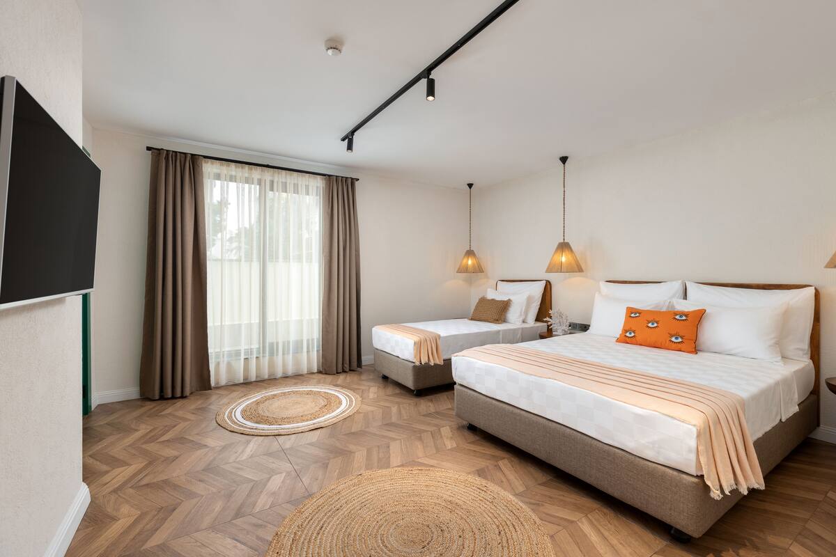A hotel room with a large bed, a smaller bed, a TV, and a window with curtains.