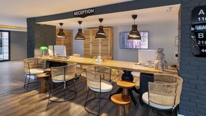 A reception area with a long wooden desk, wicker chairs, pendant lights, and a TV screen. - Azuu Bohem (Antalya)