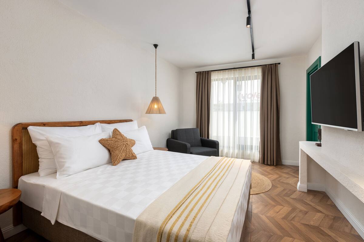 A hotel room with a large bed, a desk, a chair, a television, and a window with curtains.