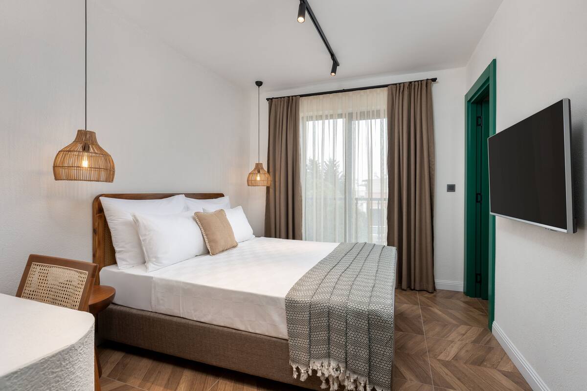A bedroom with a bed, two hanging light fixtures, a television, and a green door.