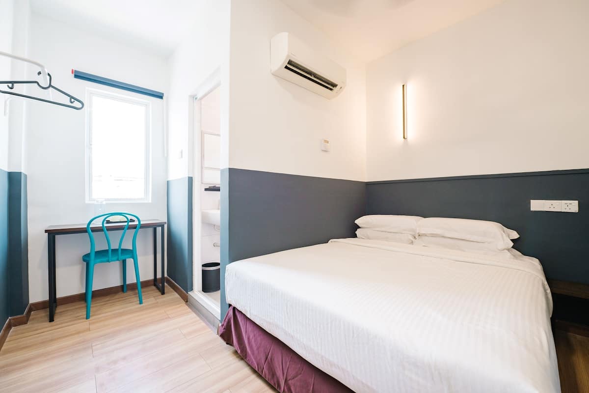 Hotellihuone, jossa on sänky, työpöytä, tuoli, ilmastointilaite ja ikkuna.
