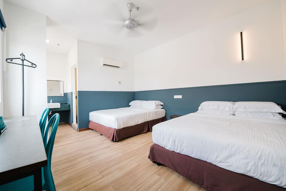 Hotellihuone, jossa on kaksi sänkyä, työpöytä, tuoli, kattotuuletin ja seinään asennettu ilmastointilaite.