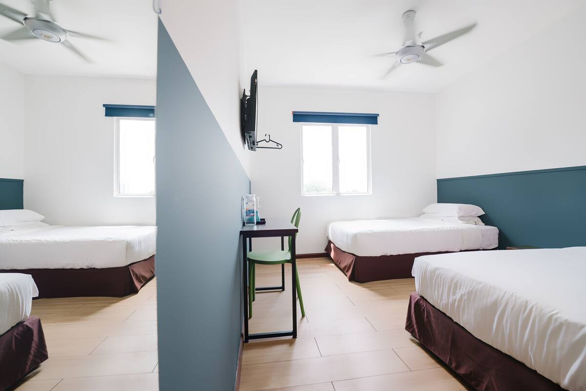 Hotellihuone, jossa on kaksi sänkyä, työpöytä tuolilla, seinälle asennettu televisio ja kaksi ikkunaa, joissa on siniset sälekaihtimet.