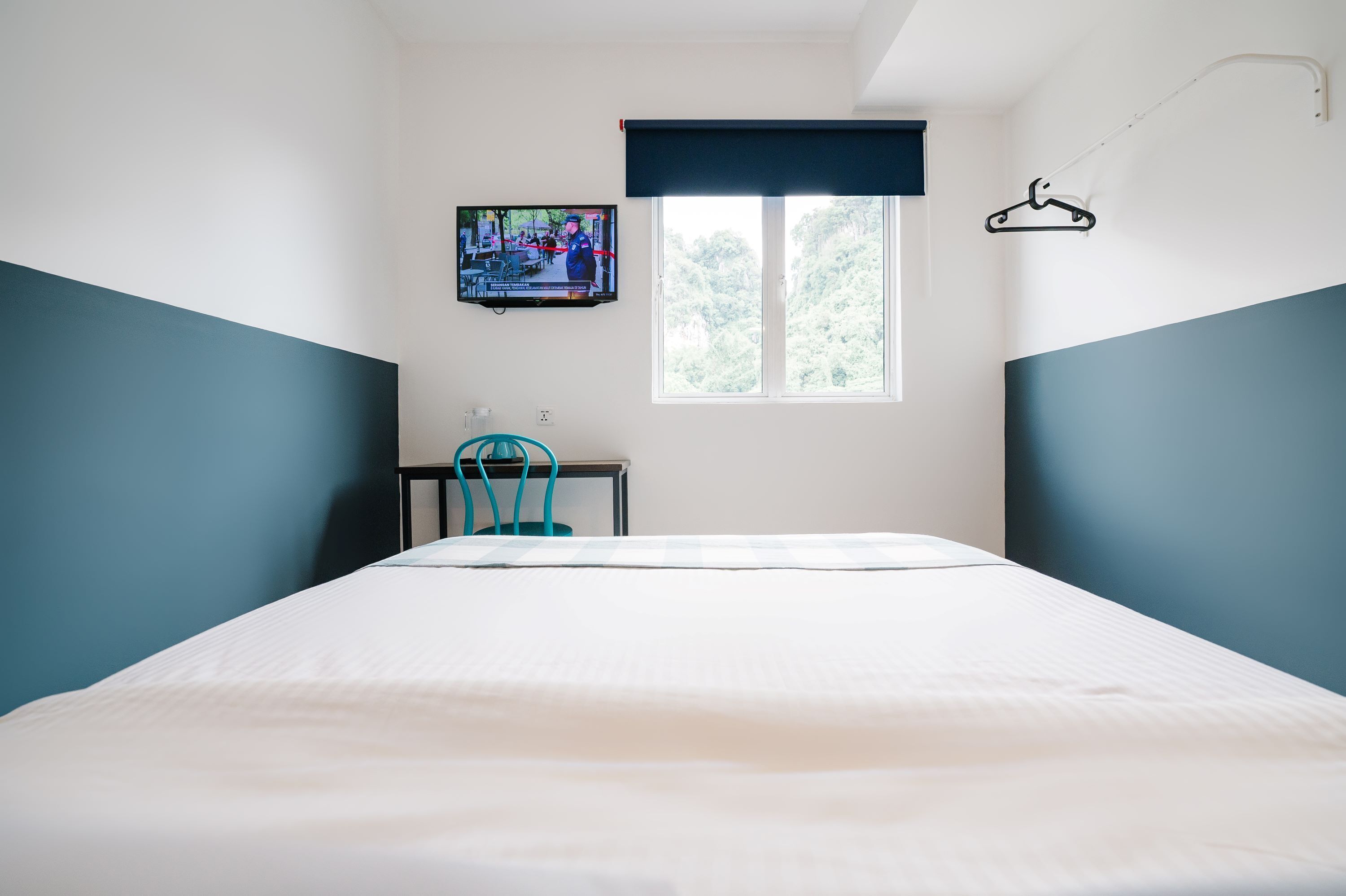 Een slaapkamer met een bed, een aan de muur bevestigde televisie, een raam met uitzicht op bomen en een kledingrek.
