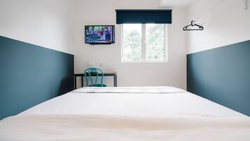 Een slaapkamer met een bed, een aan de muur bevestigde televisie, een raam met uitzicht op bomen en een kledingrek.