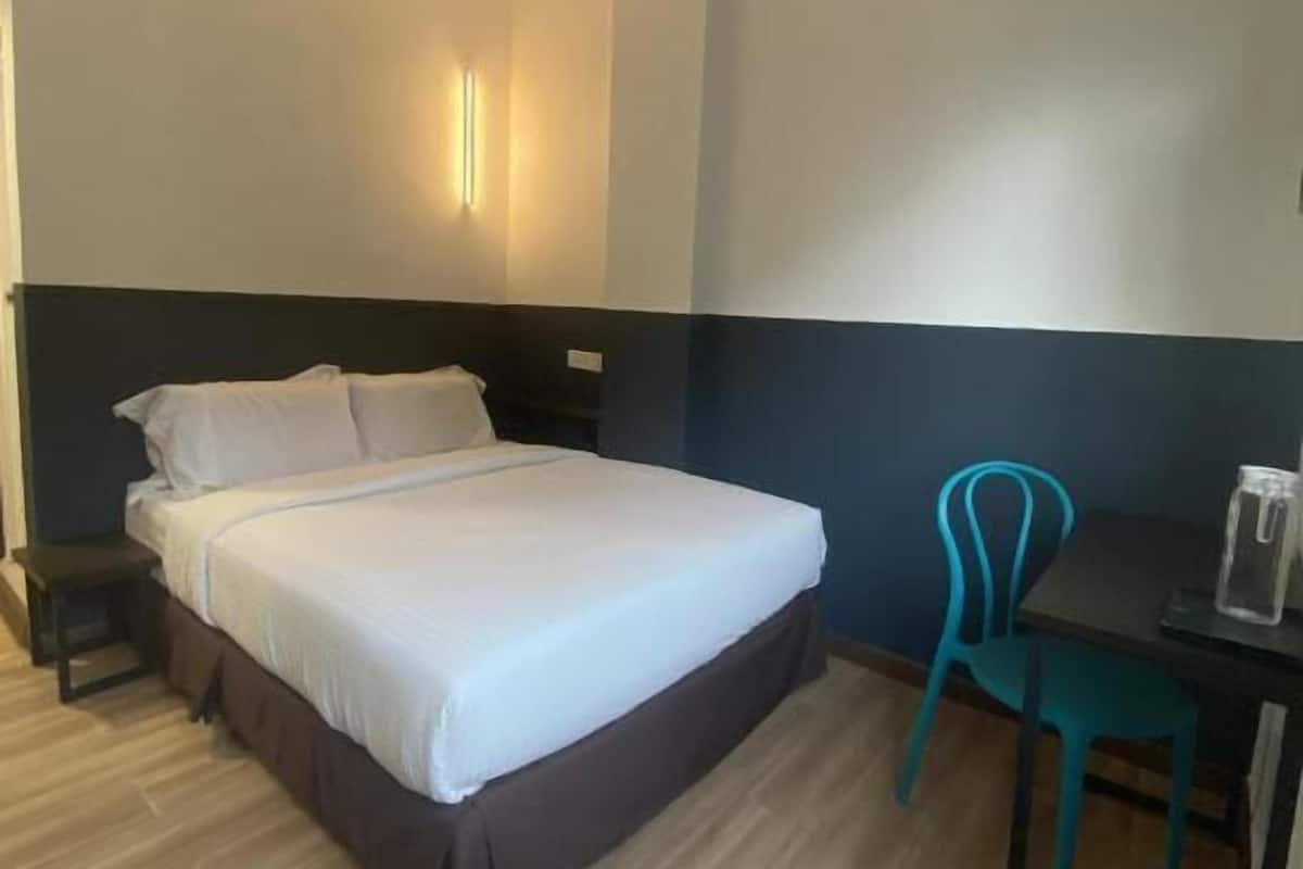 Hotellihuone, jossa on sänky, työpöytä tuolilla, kattotuuletin ja seinään kiinnitetty valaisin.