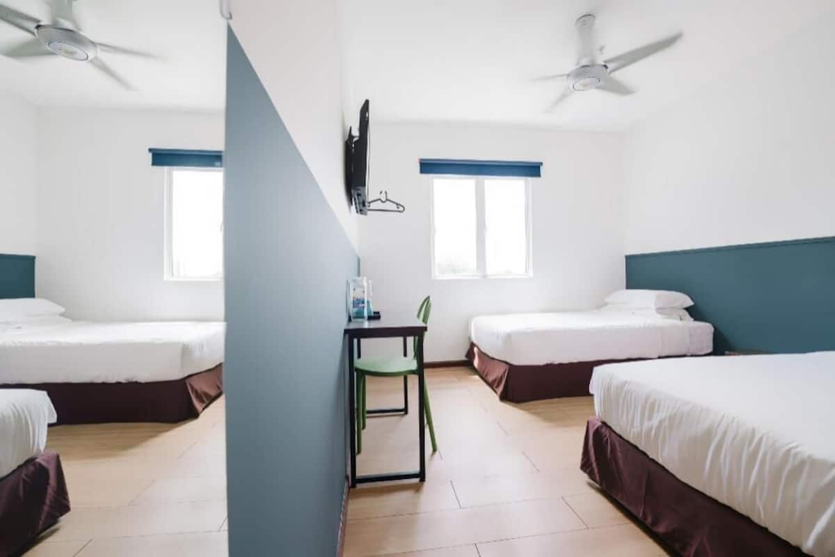 Hotellihuone, jossa on kaksi sänkyä, työpöytä tuolilla, televisio ja kaksi kattotuuletinta.
