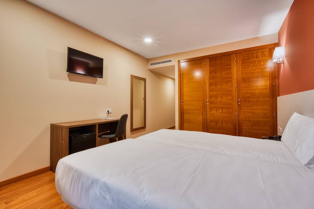 A bedroom with a bed, a desk, a chair, a TV, and a wardrobe.