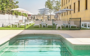 Una piscina con borde de azulejos, rodeada por una valla, y mobiliario de exterior con sombrillas.