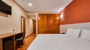 Una habitación de hotel con cama, escritorio con silla, televisión y armario.