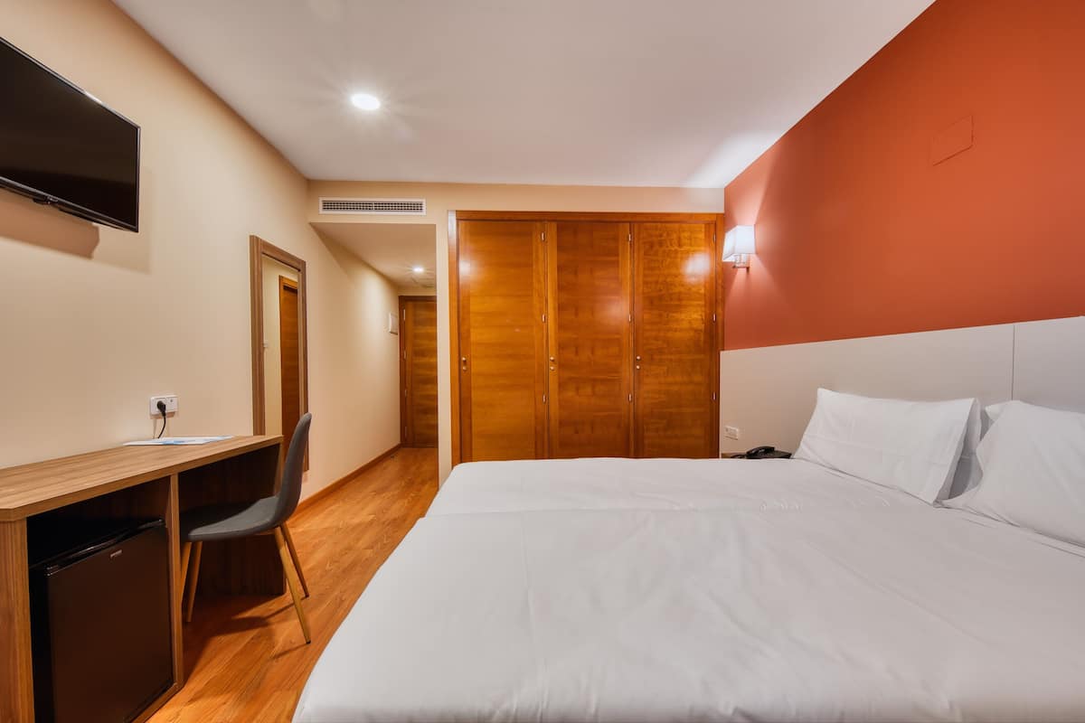 A hotel room with a bed, a desk with a chair, a television, and a wardrobe.