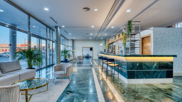 Un moderno vestíbulo de hotel con zona de bar, asientos y grandes ventanales que ofrecen vistas al exterior.