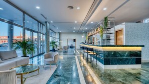 Un moderno vestíbulo de hotel con zona de bar, asientos y grandes ventanales que ofrecen vistas al exterior.