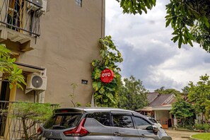 A building with a red sign, a parked car, and surrounding greenery. - OYO Capital O 90081 Pondok Sabaraya 2 Syariah (Cikampek)
