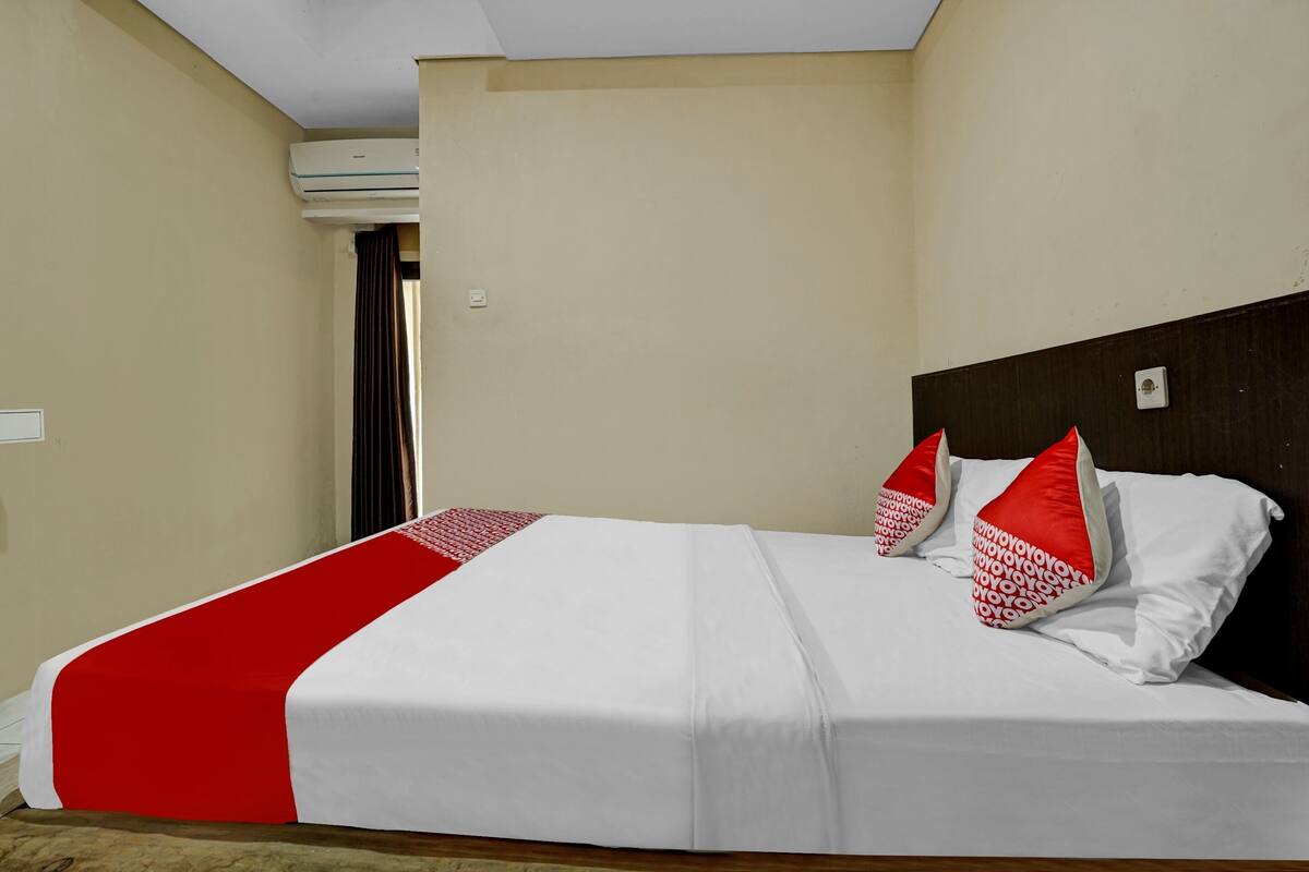 Una cama bien tendida con una colcha blanca y roja, dos almohadas rojas y un cabecero de madera.