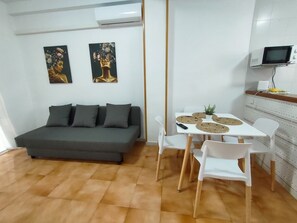 Ein modernes Wohnzimmer mit einem grauen Sofa, weißen Stühlen, einem kleinen Tisch mit gewobenen Untersetzern und zwei an der Wand befestigten Bildern.
